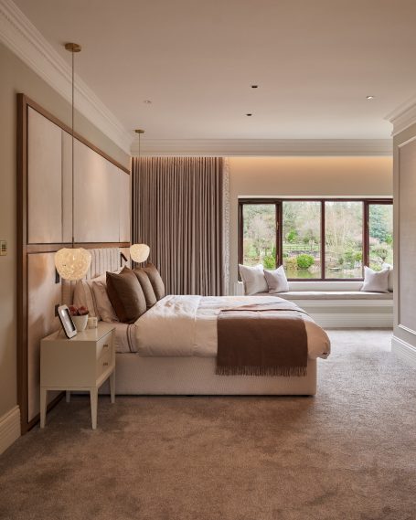 Modern bedroom with a large bed, neutral tones, and a window seat overlooking greenery.